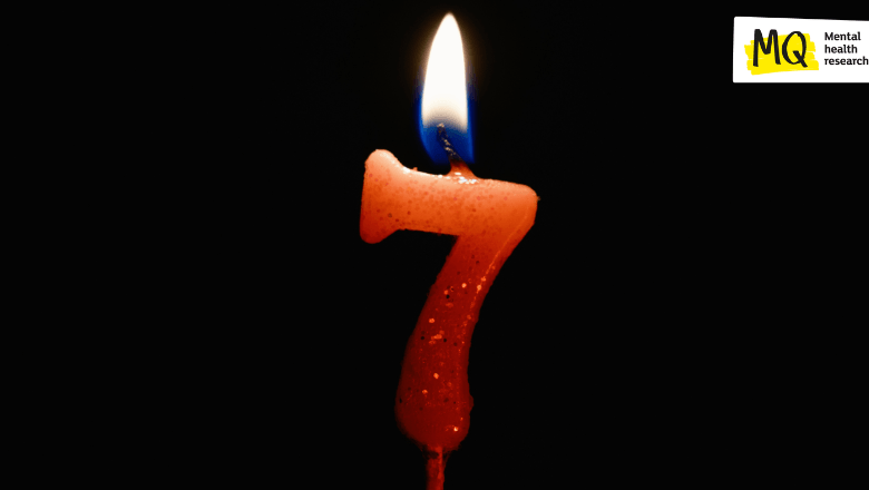 A red candle in the shape of the number 7 gently burns against a black background