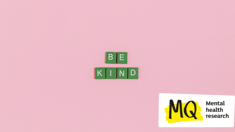The words 'be kind' are spelt out on green tiles in cream font against a pale pink background.