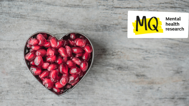 A heart shaped cookie cutter lies on a grey marble effect surface filled with red pomegranate seeds. We view it from above.