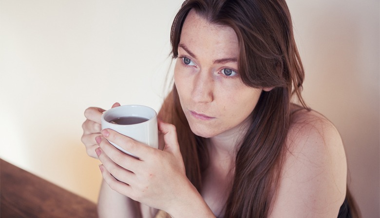A white woman with long reddish hair stares into the middle distance while holding a big of tea